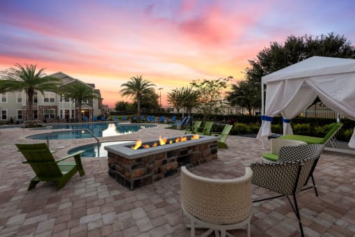 a patio with a firepit and chairs with a pool in the background