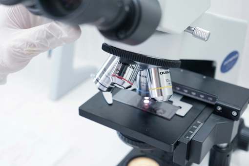 A microscope with a slide of samples being held by a gloved hand.