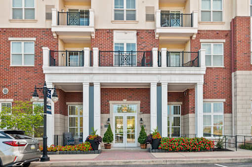A red brick building with a white balcony and a silver car parked in front.