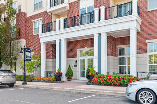 A red brick building with a white balcony and a white car parked in front.