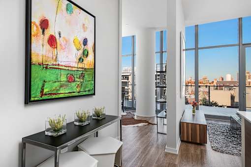 A painting of flowers is hanging on the wall above a table in a room with a view of the city.