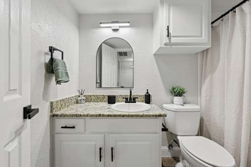 A white bathroom with a marble countertop and a round mirror.