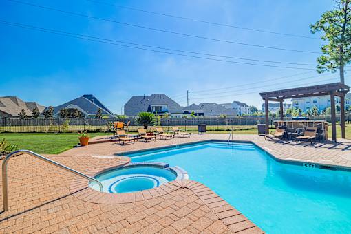 A swimming pool surrounded by a brick patio and a wooden pergola.