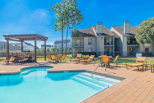 A pool with a slide and sun loungers in front of apartment buildings.