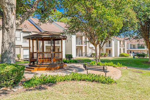 A gazebo sits in the middle of a grassy area with a bench in front of it.