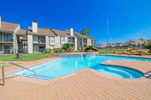 A swimming pool surrounded by a brick patio and apartment buildings.