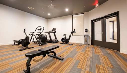 A gym with a variety of equipment including treadmills, weights, and a bench.