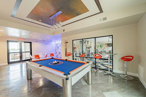 A pool table is in the middle of a room with a bar area.