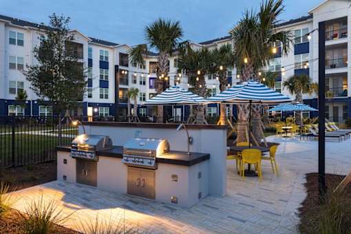 A barbecue grill is set up on a patio with yellow chairs and umbrellas.