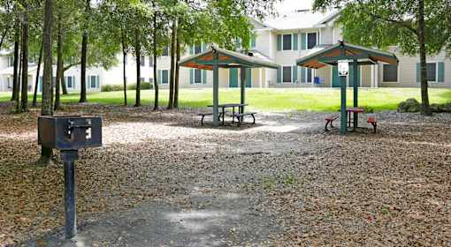 A park with picnic tables and benches in front of apartment buildings.