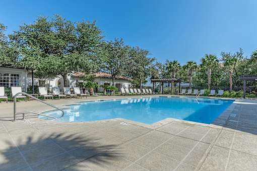 A large swimming pool surrounded by trees and lounge chairs.