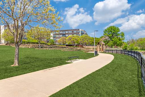 A park with a paved walkway, a bench, and a fence.