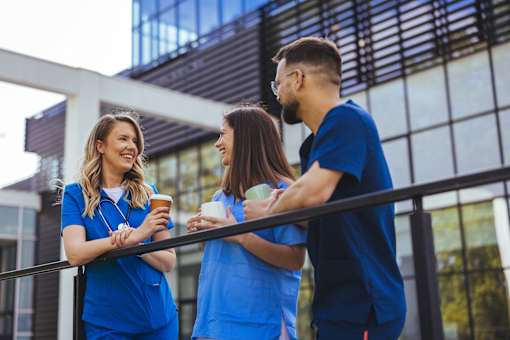 Three people in blue scrubs are standing on a balcony.