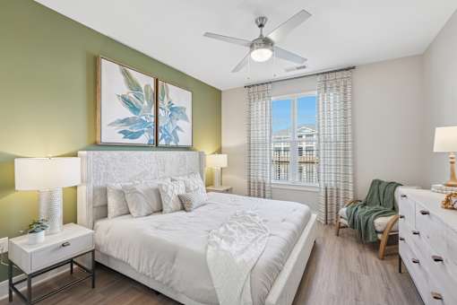 A bedroom with a large bed, a ceiling fan, and a window with a view of a building outside.