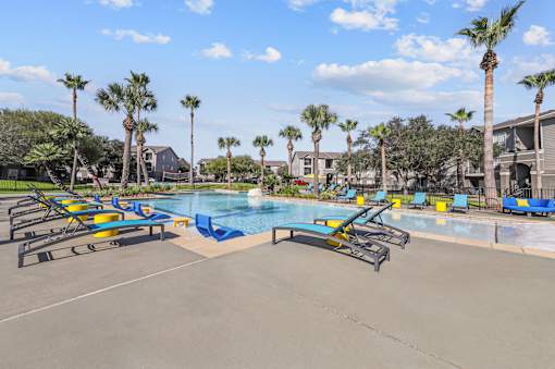 A pool surrounded by palm trees and lounge chairs.