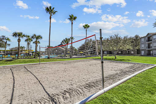 A sand volleyball court with a red net and a blue sky in the background.