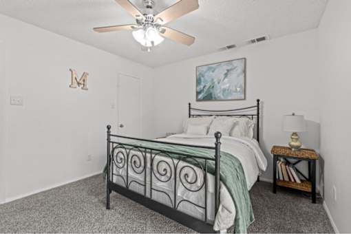 A bedroom with a bed, a ceiling fan, and a painting on the wall.