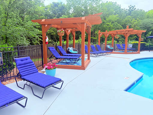 A poolside area with blue lounge chairs and a wooden pergola.