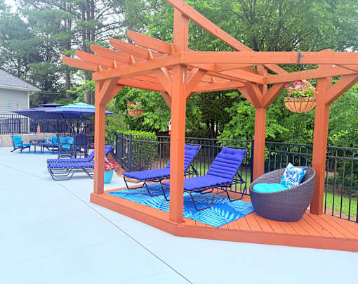 A wooden pergola with blue chairs and a wicker ottoman.
