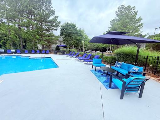A pool with a blue umbrella and chairs.
