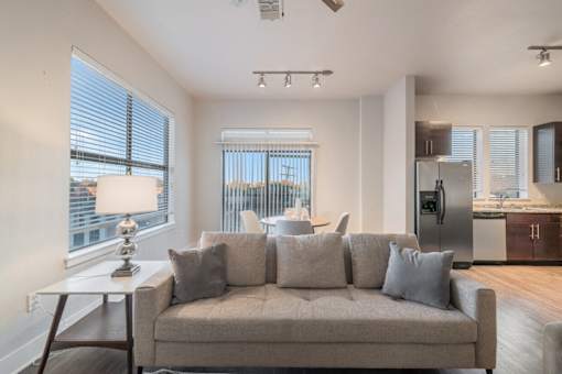A modern living room with a grey couch and a table with a lamp on it.