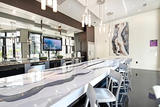 A long white marble bar with white chairs and a TV on the wall.