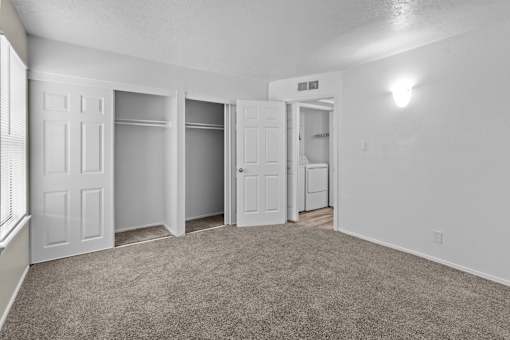 A room with white walls and carpeted floor with four doors.