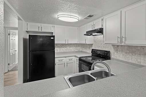 A black refrigerator is in a kitchen with white cabinets.