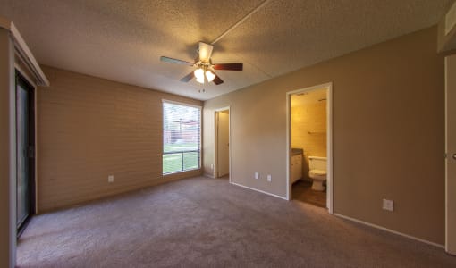 an empty living room with a ceiling fan and a door to a bathroom