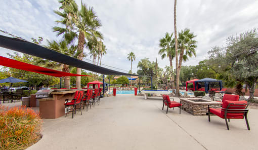 a patio with red chairs and tables and a pool with palm trees