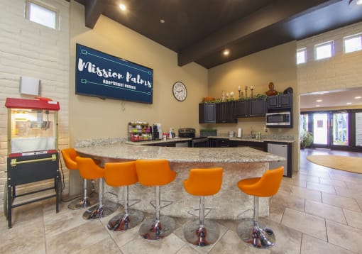 the clubhouse has a large counter with orange bar chairs and a refrigerator