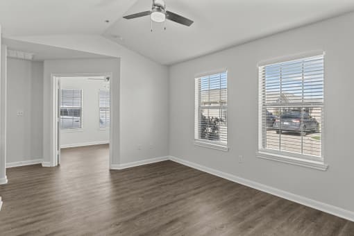 an empty living room with a ceiling fan and three windows