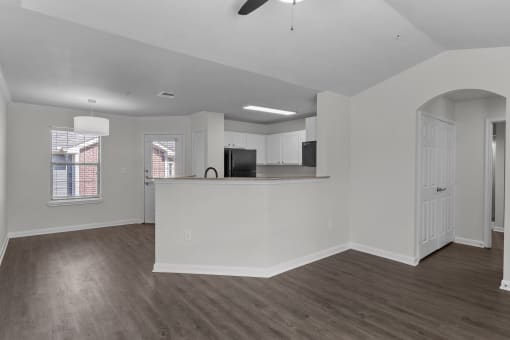 an empty living room and kitchen with a counter top and a refrigerator