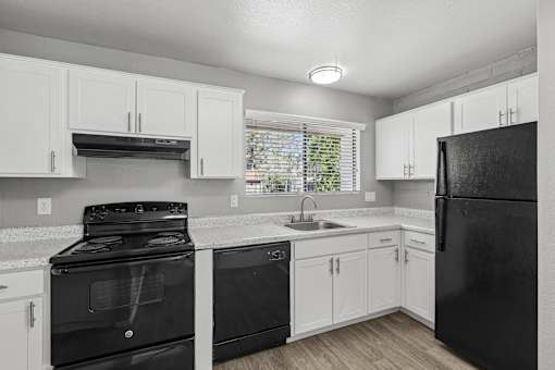 A black refrigerator sits in a kitchen with white cabinets.