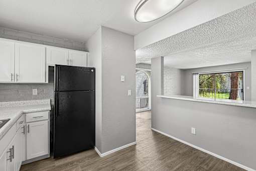 A black refrigerator sits in a kitchen with white cabinets and a window.