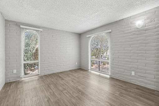 A room with white walls and wooden flooring, featuring a window with blinds and a sliding glass door.
