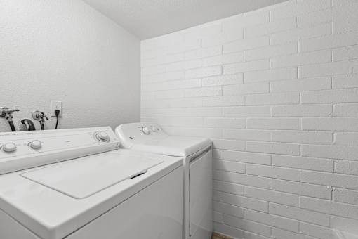 A white washing machine and dryer in a laundry room with white brick walls.