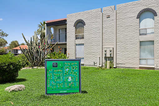 A green sign with a map on it is in the foreground of a grassy area.
