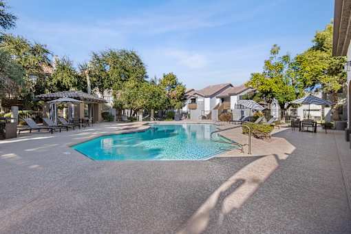A swimming pool surrounded by a concrete patio and lounge chairs.