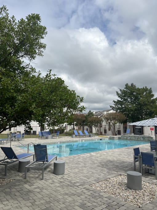 a swimming pool with blue chairs and trees and a cloudy sky