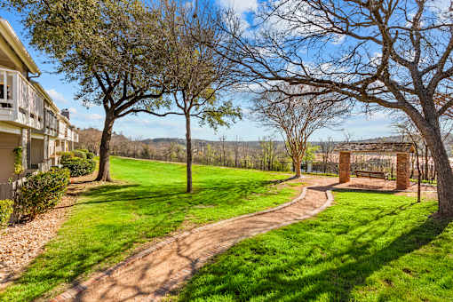 A pathway leads through a grassy area with trees and a bench.