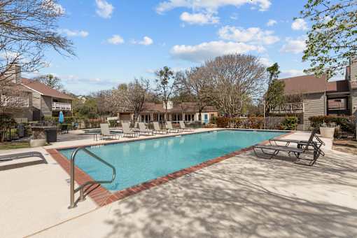 A swimming pool surrounded by a concrete patio and lounge chairs.