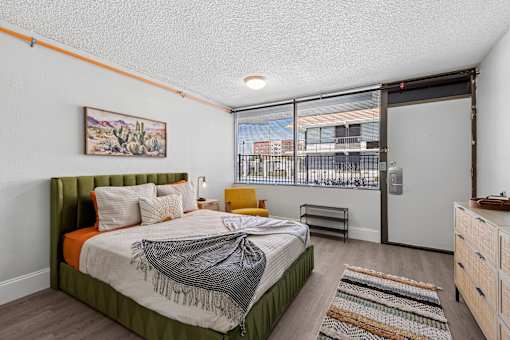 A bedroom with a bed, dresser, and window overlooking a cityscape.