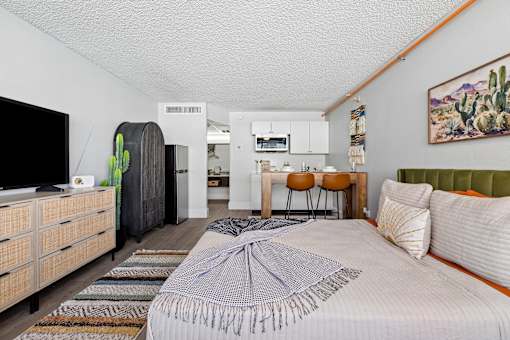 A bedroom with a bed, dresser, and a painting of a cactus on the wall.