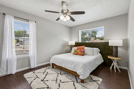 A bedroom with a bed, a ceiling fan, and a window with white curtains.
