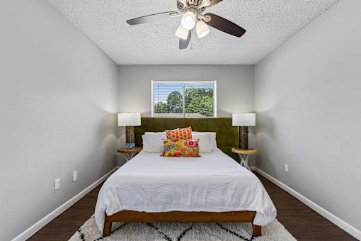 A bedroom with a bed, two lamps, and a ceiling fan.
