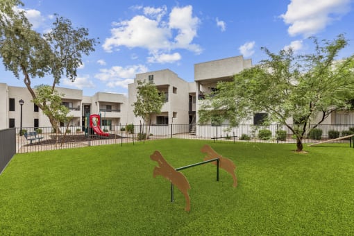 a yard with a seesaw and a dog statue in front of a building