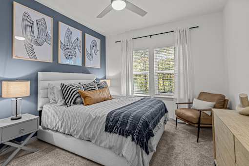 A bedroom with a bed, chair, and artwork on the wall.