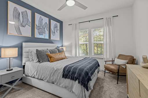 A bedroom with a bed, chair, and artwork on the wall.
