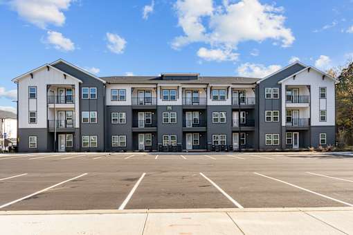 A large grey and white apartment building with a parking lot in front.